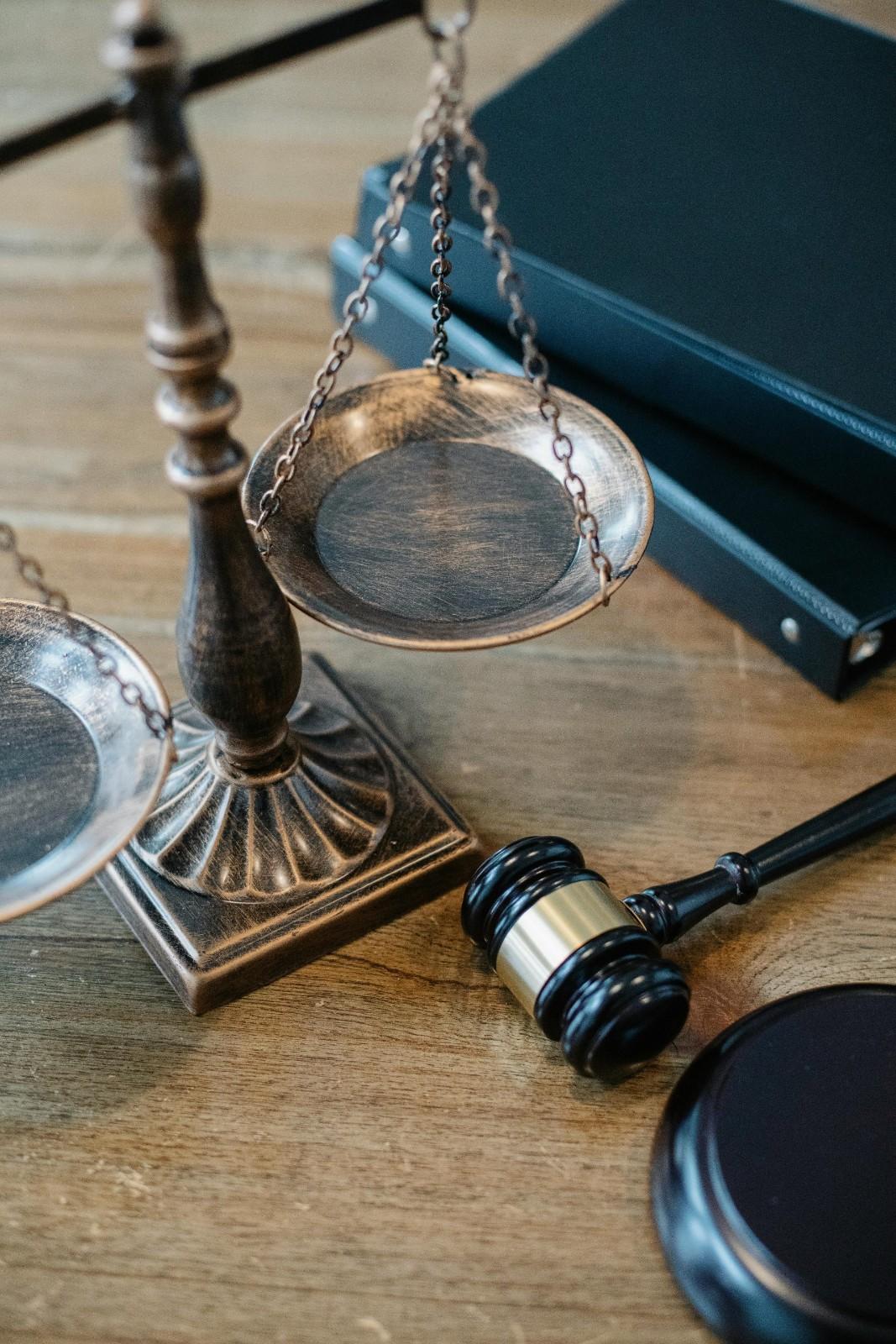 Desde arriba se muestran símbolos judiciales que consisten en una balanza de la justicia y un pequeño martillo de juez con mango rizado.